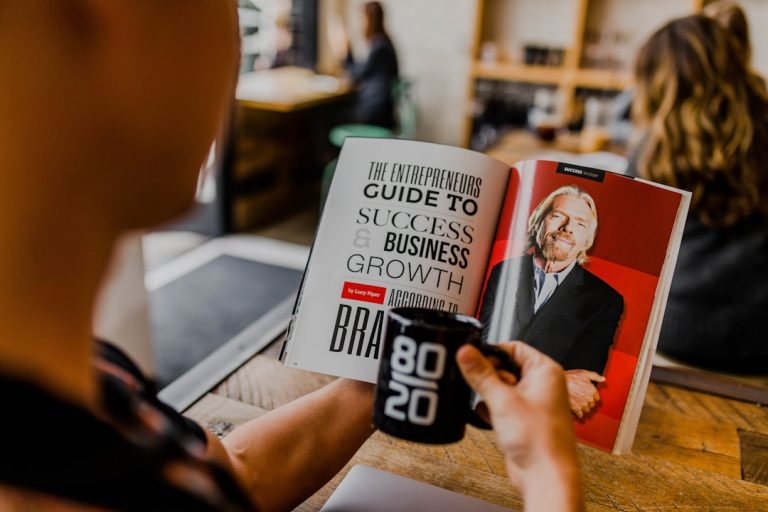 A gentleman reading a book with Richard Branson holding a mug with 80/20 displayed.